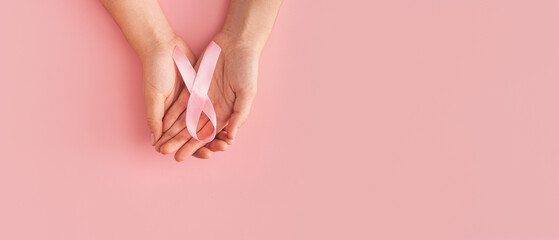 Obraz na płótnie Canvas Pink ribbon in the palms on pink background