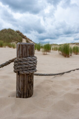 A wooden post with stretched ropes separating the hiking trail from the protected area. Photo taken in good lighting conditions on a cloudy day