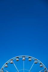 A white ferris wheel against a blue sky background. Photo taken in good lighting conditions