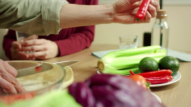 A young man is showing his friend how to cut chilly pepper properly