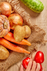 The cook's hand is choosing ingredients to prepare. Potato, red pumpkin, purple sweet potato, tomato, bottle gourd on brighten wooden background. Top view. Clean and Fresh Food. Healthy vegetables.