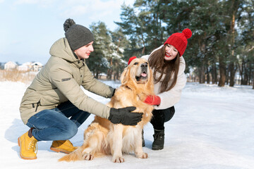 Happy young couple is played with golden retriever in winter outdoors. Walking in the forest