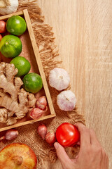 The cook's hand is choosing ingredients to prepare. Potato, tomato, dry onion, red pumpkin, ginger on brighten wooden background. Top view. Clean and Fresh Food. Healthy vegetables. Space for text