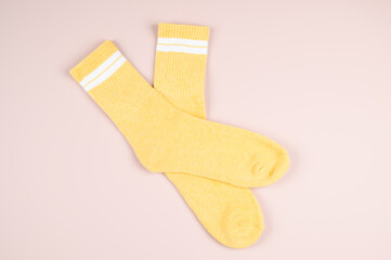 Pair of yellow socks with white strips on pastel pink background, top view