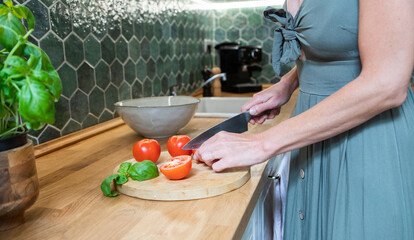 fwoman cutting fresh tomatoes and basil in modern kitchen interior with white furniture home background