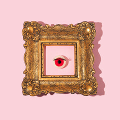 Eyeball figurine with eyelash in retro golden painting frame on pastel pink background. Halloween minimal creative concept. Pink eye fashion aesthetic idea.