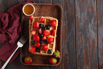 Fresh homemade Belgian waffles on an old wooden table with strawberries, blackberries and honey. Top view. Copy space.