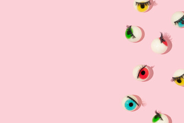 Creative pattern or frame made with eyeball figurines with eyelashes on pastel pink background. Halloween minimal creative concept. Rainbow colored eyes. Modern fashion aesthetic idea.