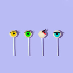 Creative layout made with eyeball lollipops with eyelashes  on pastel purple background. Halloween minimal creative concept. Rainbow colored eyes. Modern fashion aesthetic or cosmetic idea.