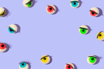 Creative pattern or frame made with eyeball figurines with eyelashes on pastel purple background....