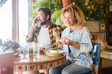 Happy adult man and woman enjoy time together eating healthy food at bar restaurant sitting at the table to lunch - hipster caucasian couple smile and spend time with each other