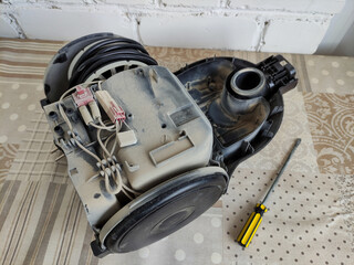 Disassembled broken vacuum cleaner and screwdriver on the table