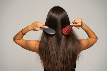 Rear view of a woman brushing her hair with two hair brushes on gray background