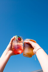 Happy young friends toasting with refreshing drinks under blue sky on summer day
