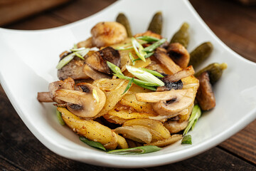Roasted potatoes with mushrooms and pickles on the wooden background