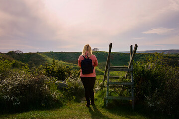 Woman walking on hiking trail during sunset in countryside landscape in Skåne, Sweden. Woman wearing outdoor clothing with a pink wind jacket and a backpack. Photo taken at Brösarps Backar, Österlen