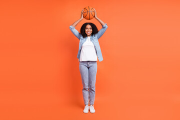 Full length photo of funky young brunette lady hold ball wear jeans shirt shoes isolated on orange background