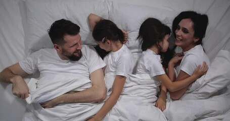 Top view of Caucasian family with two children laughing and talking in bed with white sheets. High angle shooting. A family of four is sleeping. Mom, dad and daughters good night, restful sleep 4k