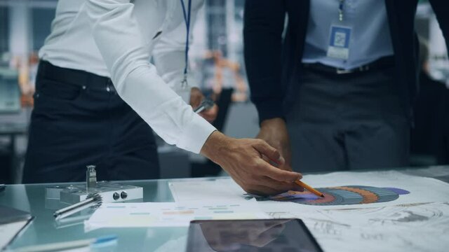 Close Up of Two Automotive Engineers Working in Office at Car Factory. Industrial Designer Shows Conceptual Electric Engine Parts to Colleague, Discussing Work in Technological Laboratory.