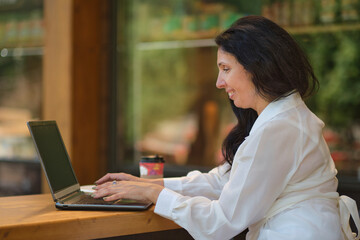 Obraz na płótnie Canvas smiling mature businesswoman drinking coffee while working in cafe