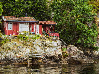 Fototapeta na wymiar Red cozy wooden house on a oslofjord rocky shore. Norwegian fjords landscape