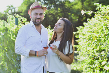 Portrait of a smiling  happy couple kissing    in a Vineyard toasting wine. Beautiful  brunette woman and bearded muscular man spending time together
