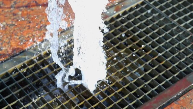 A jet of water shoots out of the ground through a metal grate.Urban modern fountain.