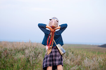 Adorable little girl with long braided hair in plaid skirt on hill with raised hands up to the sky. Happy traveler child