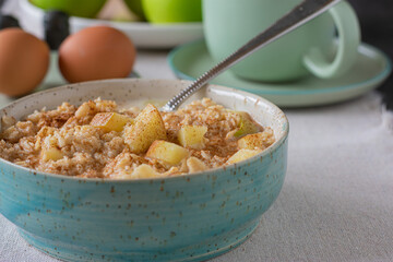 Porridge with apples and cinnamon in a bowl on kitchen table