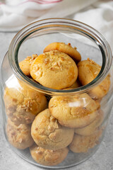 Homemade Norwegian butter cookies with almonds in a glass jar on a light gray culinary background. Traditional Scandinavian pastries closeup