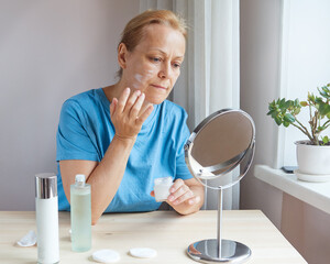 Senior woman applying nourishing anti-wrinkle cream to face skin