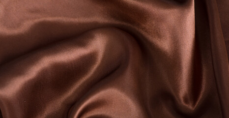 Fototapeta premium brown or chocolate silk satin fabric texture background.Cloth soft wave. Creases of satin