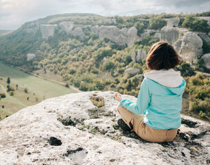 Fototapeta na wymiar The traveler sits on the edge of a cliff. Young woman resting and enjoying the beauty of nature from above.