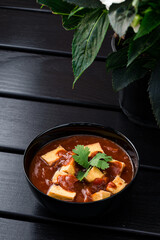 Tomato soup with cream, croutons and cilantro in a black bowl on black wooden background. Copy space for text