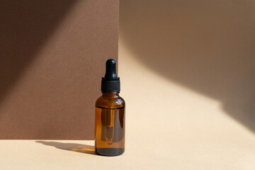 Close-up of mock-up of glass dropper bottle on abstract beige-brown background in rays of sunlight....