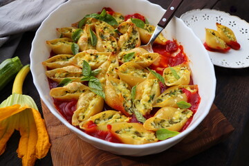 Big shell shape pasta stuffed with creamy soft cheese, zucchini and spinach sprinkled with parmesan cheese in baking dish wooden table, healthy dinner recipe, view flat lay