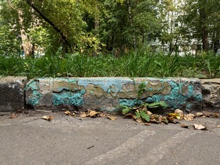Damadged old curb painted aquamarine needs to be replaced. Yellow leaves on asphalt. Front view