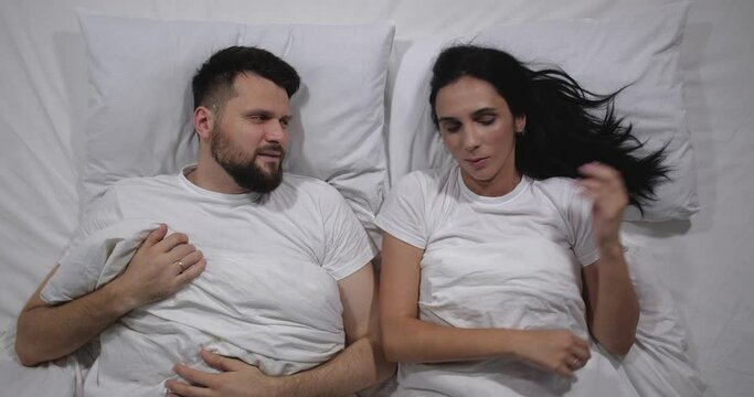  Top view of caucasian couple lying awake in bed in light room. High angle shooting.  Man amd woman looking funny videos in internet on cellphone. Social media  4k 