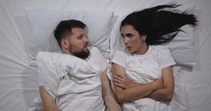 Top view of Caucasian  couple quarreling in bed with white sheets. High angle shooting. Man and woman argue, take offense at each other and turn away in different directions
