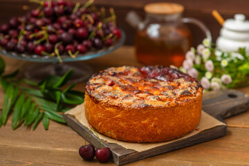 Tall cherry pie stuffed with cherry berries with intertwined ferkh lying on a board on a wooden background