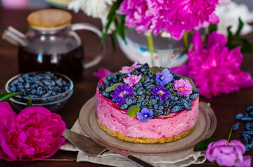 Purple cheesecake with honeysuckle, violet flowers and a background of peonies and a whole cake