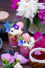 Fototapeta na wymiar Berry dessert in cups with violet flowers, macarons, and on a background of peonies