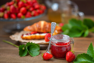 A jar of strawberry jam standing on a background of a crussan with strawberries on a wooden background