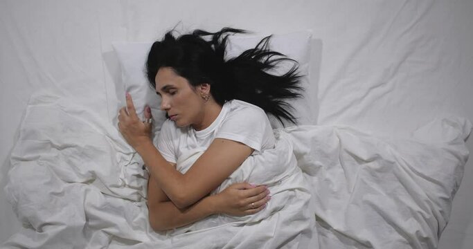  Top view of caucasian young woman waking up in bed with white linens in light room. High angle shooting. woman  waking up but raelizing that it is weekend 