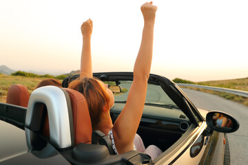 Two women in a convertible car driving raising arms