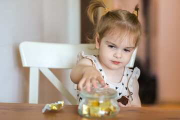 A two-year-old girl reaches for a chocolate candy from a jar. Should children be allowed to eat sweets? the effects of sugar on health