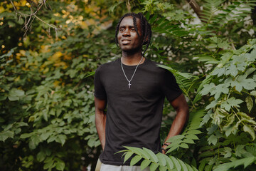 Portrait African man in black t-shirt with dreadlocks in green leaves