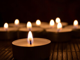 Burning candles in the dark, close up and selective focus. Copy space. Memorial concept with tea lights on wooden background