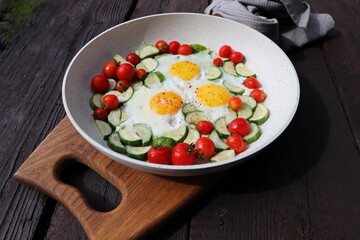 Late breakfast , fried eggs with zucchini, cherry tomaroes. Shakshuka in frying pan on rustic background. Arabic cuisine. Kosher food.