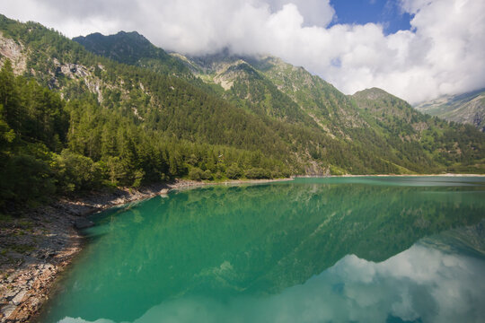 Enchanted view of the Lago dei Cavalli, Alpe Cheggio. The clear water, the rich vegetation, the blue sky and the white clouds during summer season, Piedmont, Italy